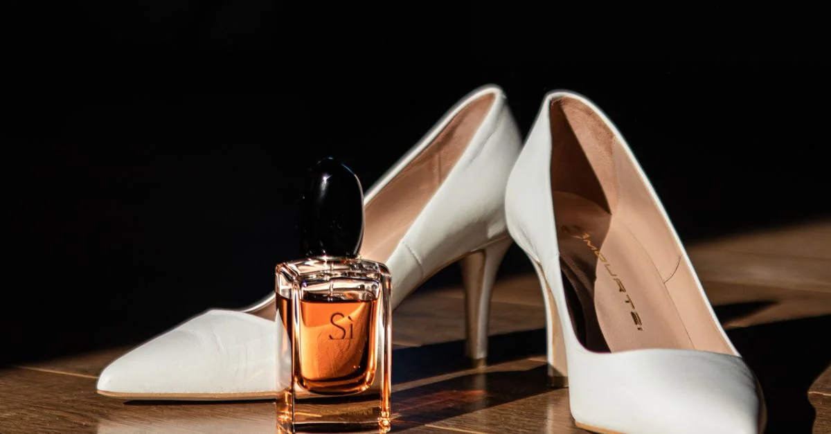 Elegantes tacones altos blancos junto a una botella de perfume de lujo en un suelo de madera.