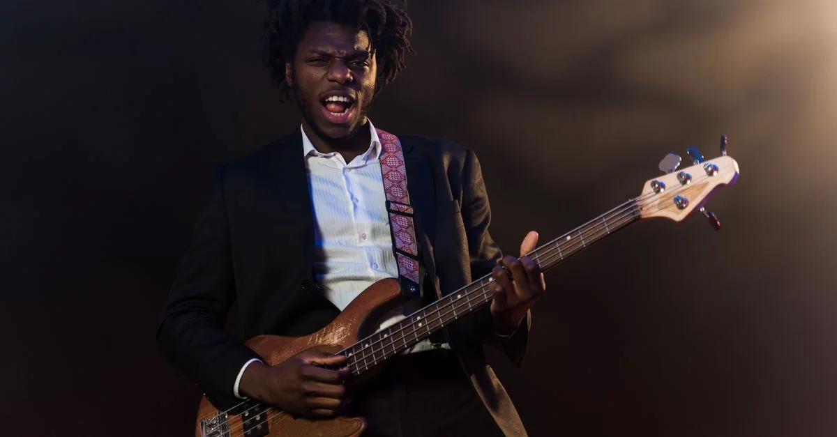 Guitarrista afroamericano enérgico actuando con guitarra eléctrica en el escenario con un traje formal.