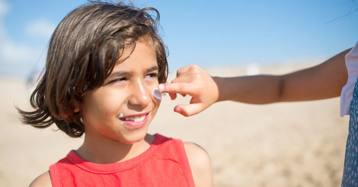 Niña con protector solar en la cara en una playa soleada, disfrutando de un día de verano al aire libre en Portugal.