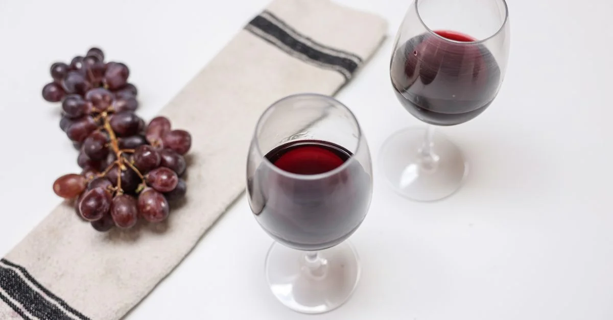 Dos copas de vino y un racimo de uvas elegantemente dispuestos sobre una mesa blanca con una servilleta.
