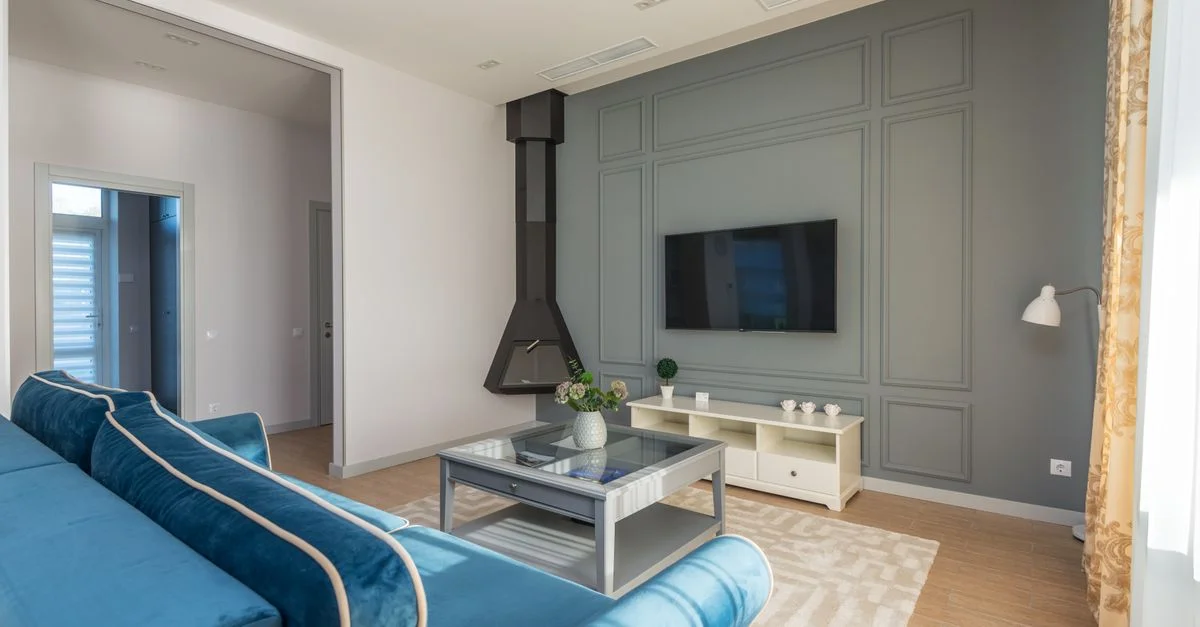 Una sala de estar elegante con un sofá azul, TV montada en la pared y decoración elegante.
