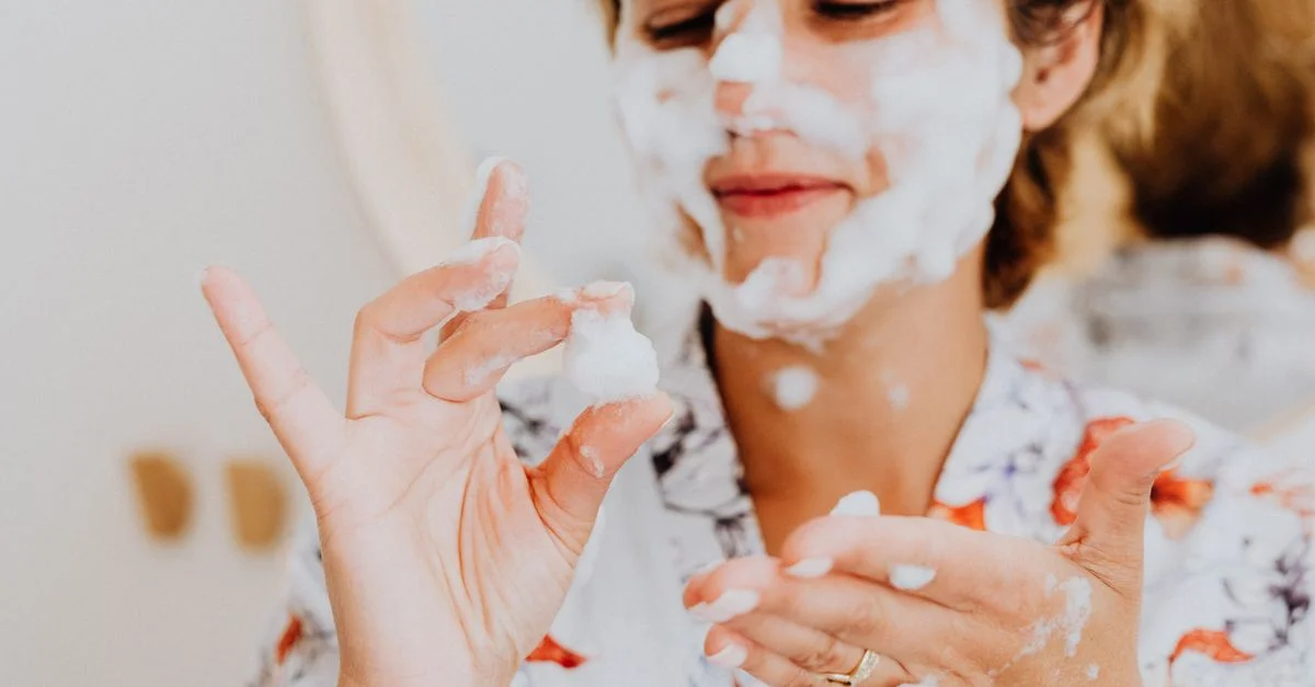Mujer divirtiéndose con una máscara facial de burbujas durante su rutina de cuidado de la piel, sonriendo y aplicando espuma en su cara.