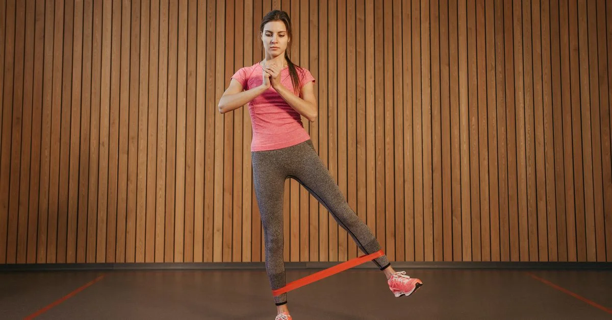 Una mujer realiza ejercicios de piernas con una banda de resistencia en un gimnasio, promoviendo el fitness y un estilo de vida saludable.