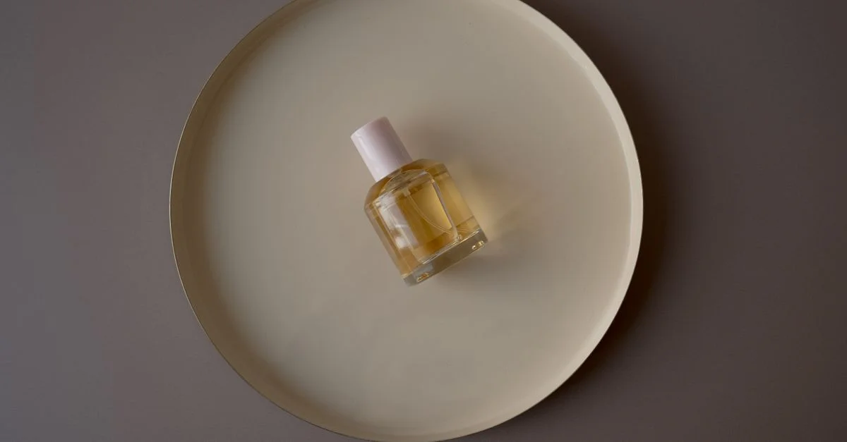 Un frasco de perfume elegantemente colocado sobre una bandeja circular beige contra un fondo gris.